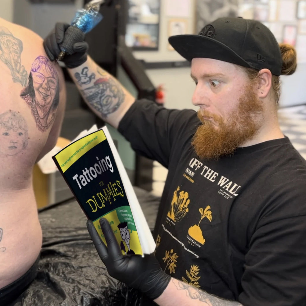 Kevin McNulty tattooing and reading a tattooing for dummies book at 7th Circle tattoo & Piercing in Oldham